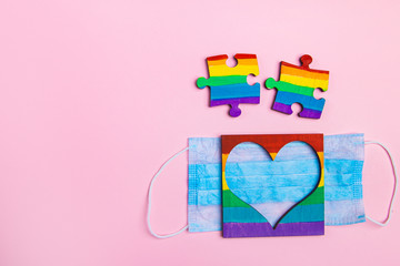 Fototapeta na wymiar LGBT symbol puzzles and heart frame painted by a rainbow on a medical mask. Coronavirus quarantine, online festival and pride day 2020. copy-space. space for text on a pink background