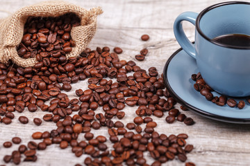 Cup of coffee and bag with coffee grains on a wooden surface