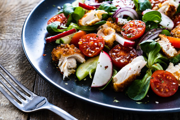 Caesar salad - fried chicken breast and vegetables on wooden table
