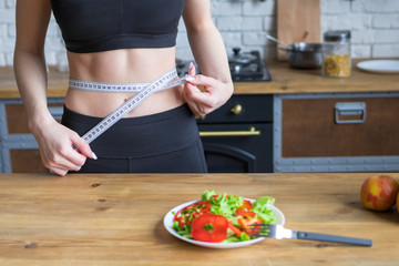 Weight loss concept, girl measures waist in the background of a plate of salad
