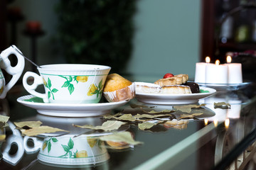 Cup of tea, cookies and candles on glass table in a living room
