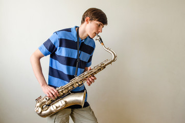 Young saxophonist plays tenor saxophone in a striped blue shirt on a white background
