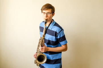 Naklejka premium Young saxophonist plays tenor saxophone in a striped blue shirt on a white background 
