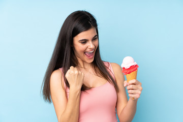 Young woman holding a cornet ice cream over isolated blue background celebrating a victory