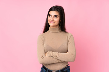 Fototapeta premium Young woman over isolated pink background looking up while smiling