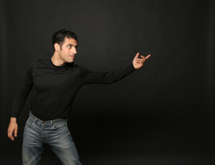 ragazzo con maglia nera e jeans compie il gesto di lanciare qualcosa con l mano, isolato su sfondo nero