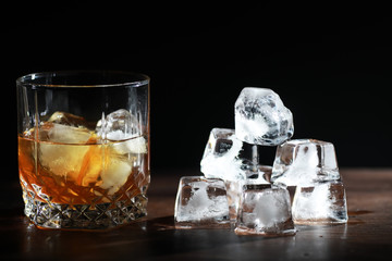 A glass of strong alcoholic drink with ice on a wooden bar counter. Whiskey with ice cubes. Glass with a chilled drink.
