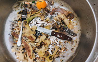A metal sink in which there are two forks, a knife with a wooden handle and potato peel. The...