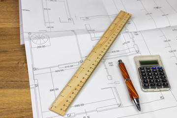 desk with building construction plan resting on top with ruler, pencil and calculator