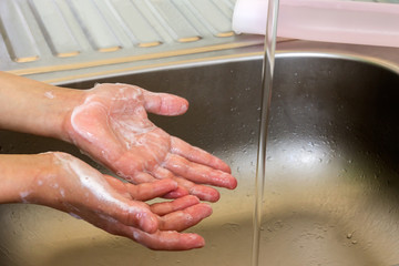 Fototapeta premium The soaped hands of a little girl, liquid soap and a stream of water from the tap in the sink.
