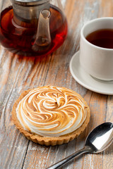 Close up of tartlet with lemon curd and burnt meringue, served with a cup of black tea