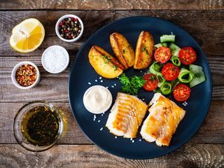 Fish dish - fried cod fillet with vegetables on wooden table
