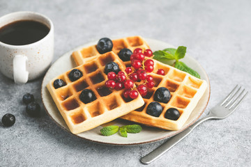 Belgian waffles with berries and cup of coffee on concrete background. Sweet breakfast food
