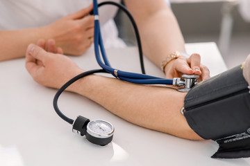The doctor uses a sphygmomanometer with a stethoscope to check the patient's blood pressure in the hospital.