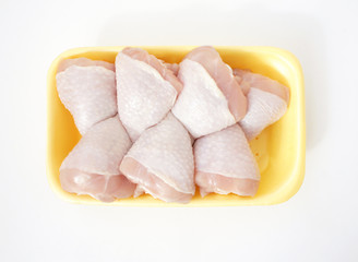 Chicken legs in a yellow polystyrene container. Set of seven raw chicken legs for cooking on light background. Top view.