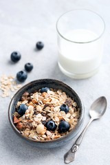 Muesli with blueberries and glass of milk on grey concrete table. Healthy food, clean eating, dieting concept