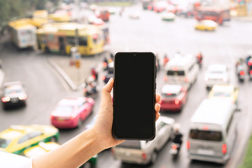 Hand holding mobile phone, city traffic jam background. close up and copy space