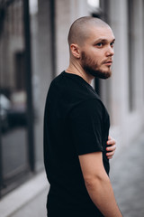 portrait of a bald handsome bearded man in a black t-shirt on the street, who looks away