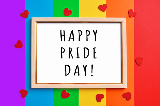 wooden frame with blank white copy space on multicolored rainbow flag background and little red hearts.