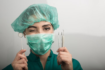 dentista con mascherina verde cuffietta verde e camice verde che mostra i suoi strumenti di lavoro...