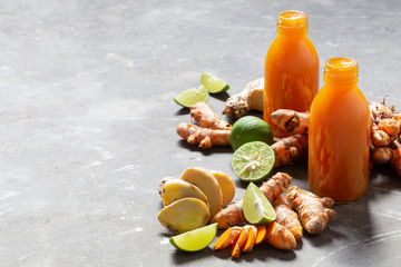 Healthy drink from turmeric and ginger roots and lime in small bottles on grey concrete background.
