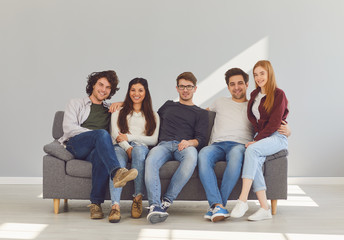 A group of friends is sitting on couch in a room on a gray background.
