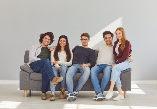 A Group Of Friends Is Sitting On Couch In A Room On A Gray Background.