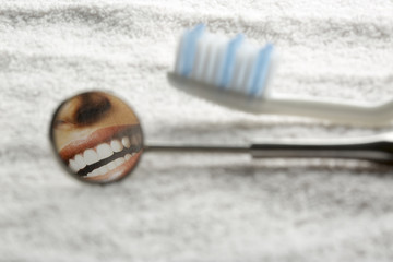 Spazzolino e specchio dentale con sorriso brillante riflesso,  su sfondo asciugamano bianco