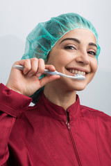 dentista con cuffietta verde in testa e camice rosso ci mostra come ci si lava i denti