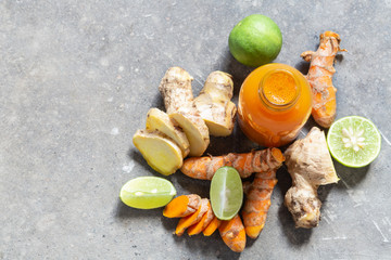Healthy drink from turmeric and ginger roots and lime in small bottles on grey concrete background.