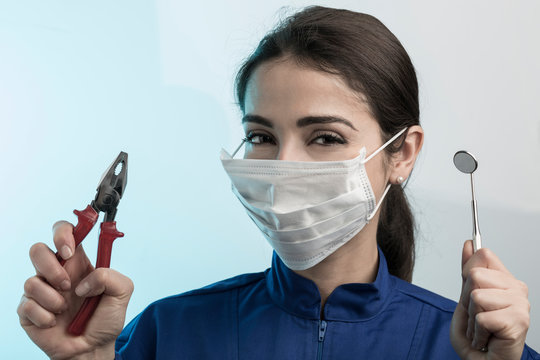 Dentista donna con mascherina chirurgica e camice blu mostra gli strumenti di lavoro in un amano e nell'altra una pinza da bricolage, isolata su sfondo celeste