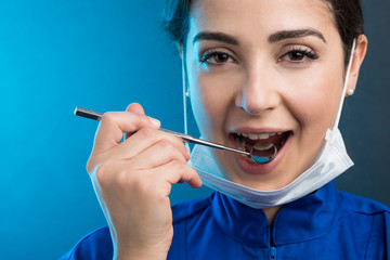 Dentista donna con mascherina chirurgica e camice blu mostra gli strumenti di lavoro, isolata su...