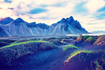 Fototapeta na wymiar Scenic landscape with most beautiful mountains Vestrahorn on the Stokksnes peninsula and cozy lagoon with green grass on the sand dunes at sunset in Iceland. Exotic countries. Amazing places.