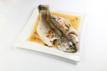 Thai style steam sea bass barramundi with lemon garlic chilli clear sauce on white serving dish