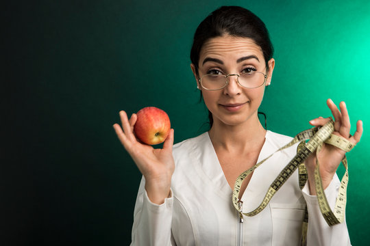 Dietologa con camice bianco mostra una mela come alimento sano per una dieta equilibrata, isolata su sfondo verde