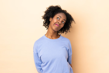 Young African American woman isolated on beige background and looking up