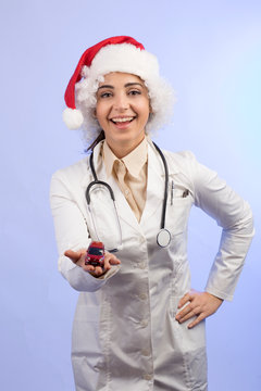 dottoressa in camice bianco , Stetoscopio intorno collo e con il cappello da babbo natale, mostra una machinetta giocattolo rossa,  isolata su sfondo celeste