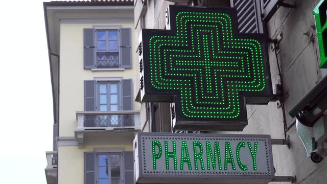 Europe, Italy , Milan April ,2020 -  pharmacy green neon sign during covid19 Coronavirus outbreak - open store in downtown of the city - San Babila square 24/7 days
