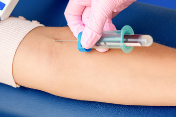 Nurse takes blood sampling introducing a needle into a vein of woman's arm.