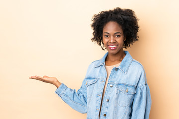 Young African American woman isolated on beige background presenting an idea while looking smiling towards