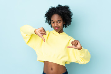 Young African American woman isolated on blue background showing thumb down with two hands