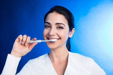 ragazza in camice bianco mostra come lavarsi bene i dento con uno spazzolino, isolata su sfondo blu - obrazy, fototapety, plakaty