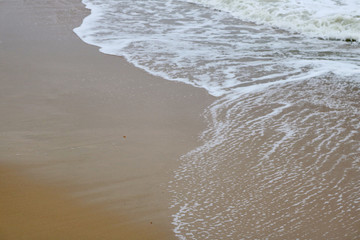 The ordinary photo of sandy beach and the sea wave with lots of white bubbles