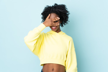 Young African American woman isolated on blue background covering eyes by hands and smiling