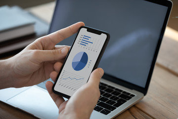 Close up businessman holding phone with graphs and diagrams on screen, analyzing startup project...