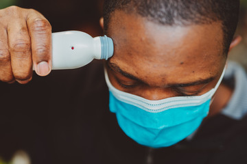 African american man using a temporal thermometer to record his temperature by running it across...