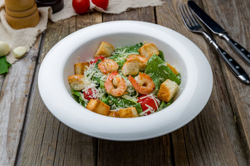 salad caesar with shrimps on white plate on wooden table