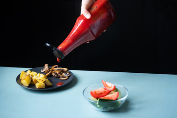 Unhealthy and healthy food nearby on a blue table. Home - fried potatoes and mushrooms watered with ketchup
