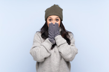 Young Colombian girl with winter hat over isolated blue background with surprise facial expression