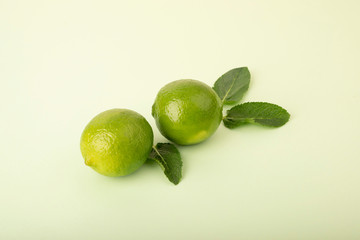 Fresh green limes on a pastel background. Mint leaves are laid out in the background and complement the composition. Whole fruits and halves lie on a wooden base. Fruit layout of lime and mint.